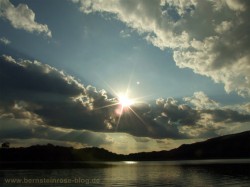 Golden glitzernder See mit schillernder Sonne und Wolken.